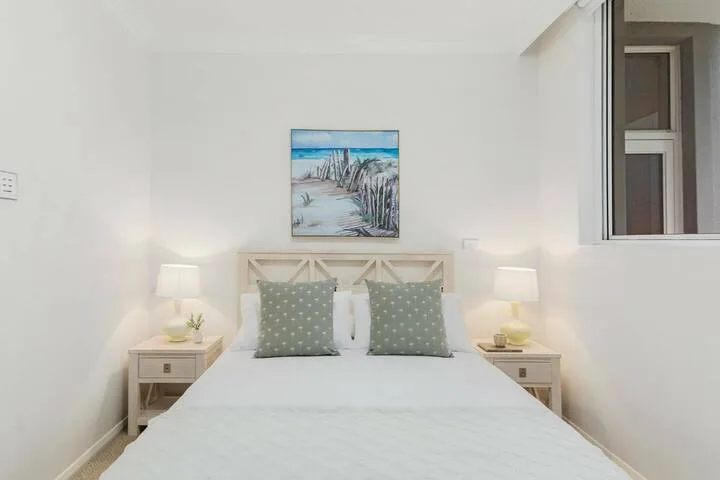 Un dormitorio luminoso con una cama bien tendida y un cuadro de playa encima.