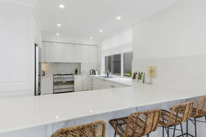 Una cocina blanca y luminosa con una isla amplia y asientos tejidos.