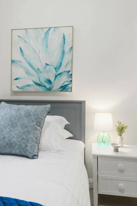 Un dormitorio con una cama arreglada, arte enmarcado y una mesita de noche.