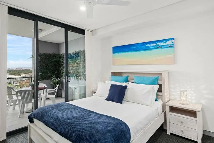 Un dormitorio luminoso con una cama, ropa de cama azul y una puerta corrediza de vidrio.