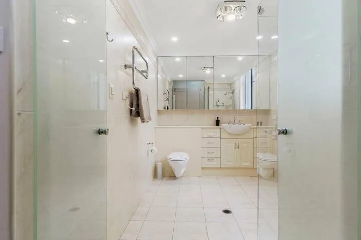 Un baño luminoso con azulejos, lavabo, espejo e inodoro.