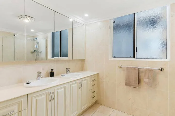 Un baño luminoso con un tocador largo, armarios con espejo y una ventana esmerilada.