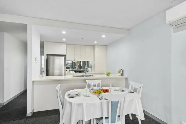 Un comedor luminoso con una mesa redonda puesta frente a una cocina abierta.