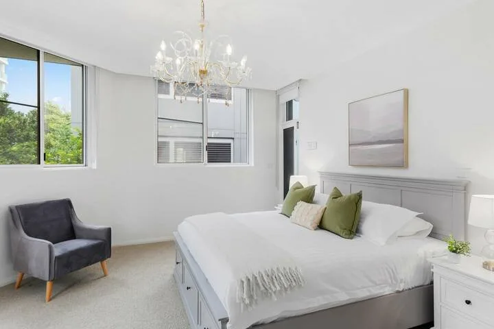Un dormitorio luminoso con cama, asientos acolchados y ventanas grandes.