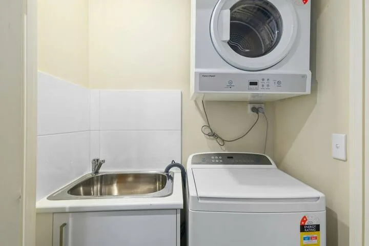Una zona de lavandería con un fregadero de acero inoxidable y lavadoras apiladas.