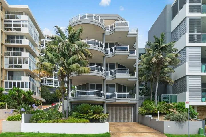 Un edificio de apartamentos moderno está rodeado de palmeras y vegetación ajardinada.