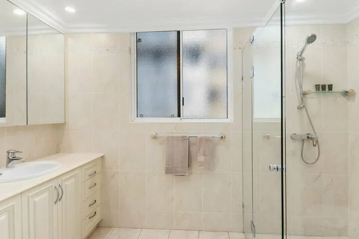 Un baño de azulejos con lavabo, ventana esmerilada y ducha de vidrio.