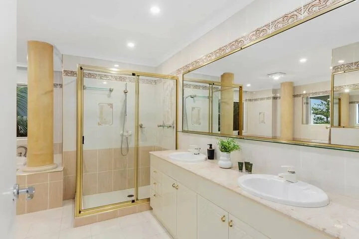 Un baño luminoso con ducha de vidrio y un largo tocador con lavabos.