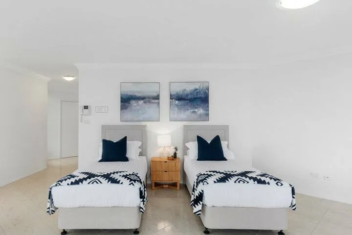 Un dormitorio luminoso con dos camas individuales y cuadros abstractos sobre los cabeceros.