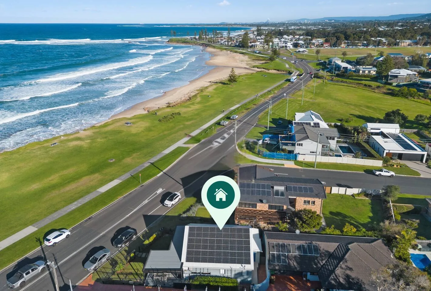 Vista aérea de la costa, con olas junto a una playa de arena, una carretera y edificios.