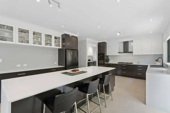 Una cocina moderna con una isla larga y gabinetes oscuros.