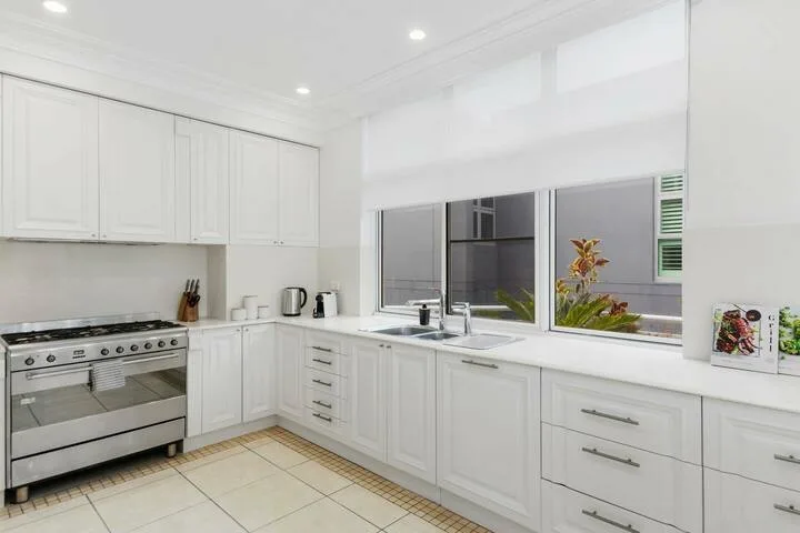Una cocina luminosa con gabinetes blancos, una encimera y ventanas amplias.