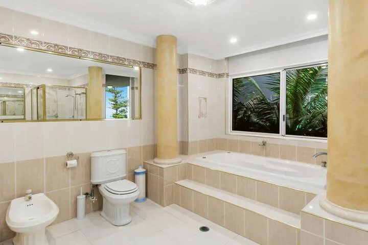 Un baño amplio con bañera, inodoro y grandes ventanas con vistas a la vegetación.