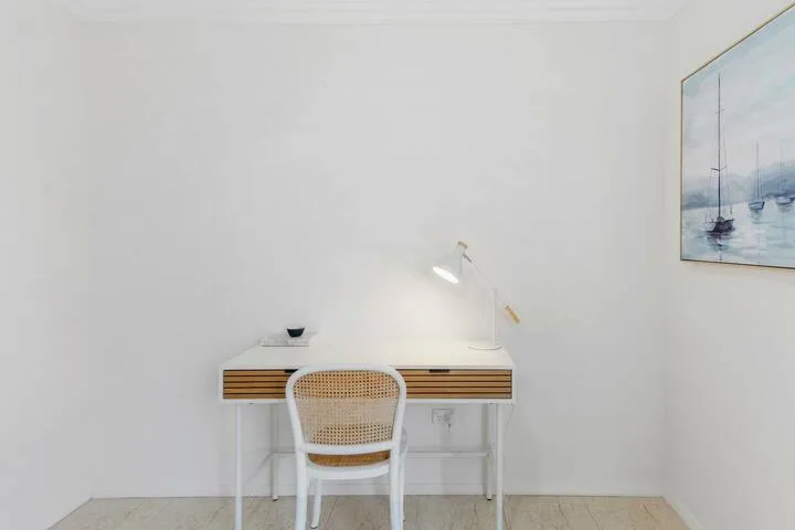Un escritorio y una silla están frente a una pared lisa, bajo un cuadro de veleros.