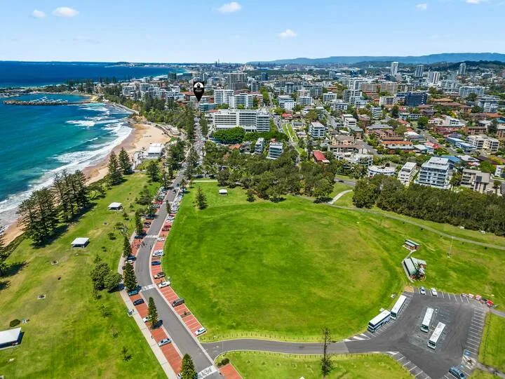 Vista aérea de una ciudad costera con un campo ovalado verde junto a la playa.