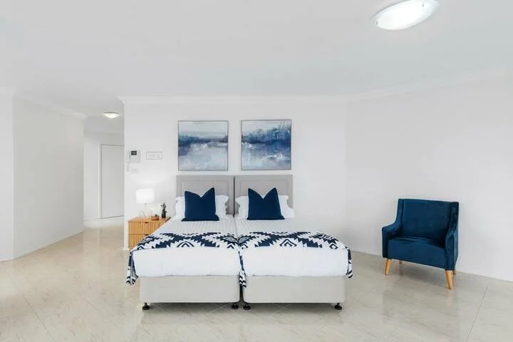 Un dormitorio luminoso con dos camas y un sillón azul.