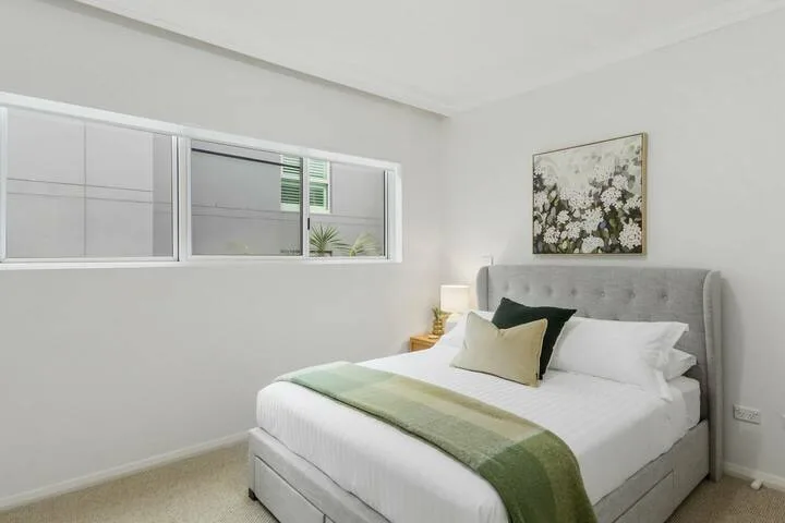 Un dormitorio luminoso con una cama tendida y una ventana amplia.