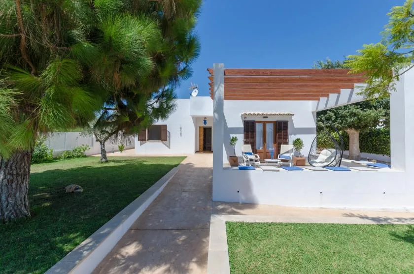 Una casa blanca y un patio exterior junto a un camino pavimentado y césped verde.