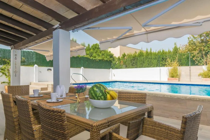 Una zona de estar en un patio cubierto da a una piscina y un jardín.