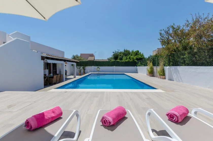 Una piscina al aire libre está junto a una amplia terraza soleada.