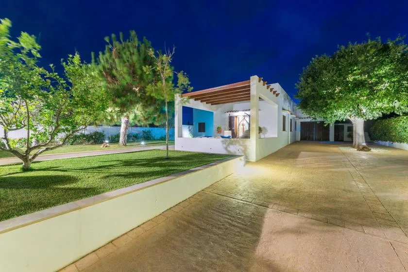 Una casa moderna está junto a un césped ajardinado y una entrada pavimentada por la noche.