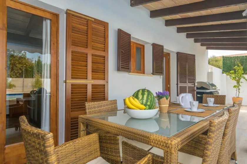 Un comedor exterior cubierto tiene una mesa de vidrio y asientos tejidos.