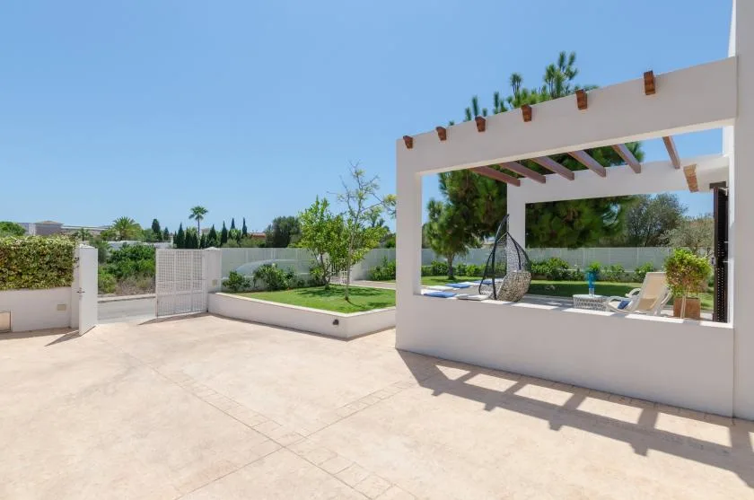 Un patio soleado con pérgola, asientos de descanso y una pequeña zona de césped.