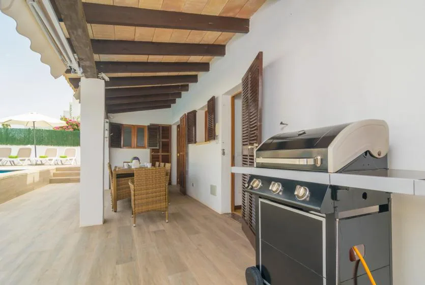 Un patio cubierto con una parrilla y asientos de mimbre junto a la piscina.