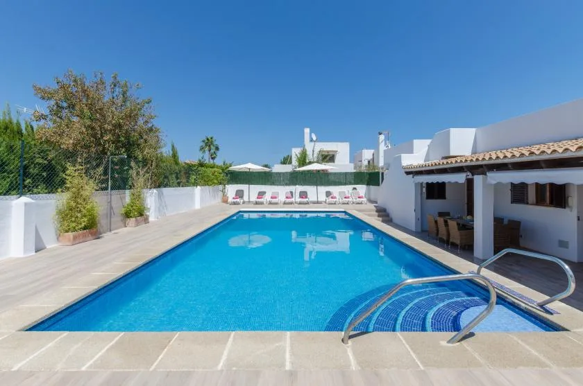 Una piscina al aire libre junto a un edificio blanco, con tumbonas al fondo.