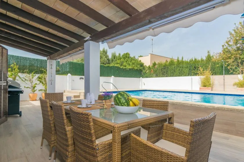 Un patio cubierto con asientos de mimbre y una mesa da a una piscina.