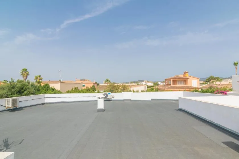 Una terraza plana en la azotea, con muros bajos blancos y casas a lo lejos.
