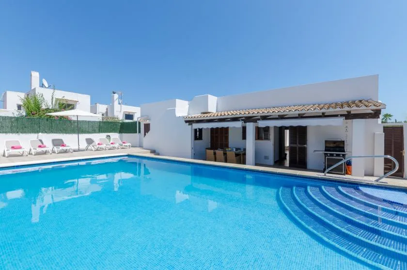 Una piscina al aire libre junto a un edificio blanco con un patio sombreado.
