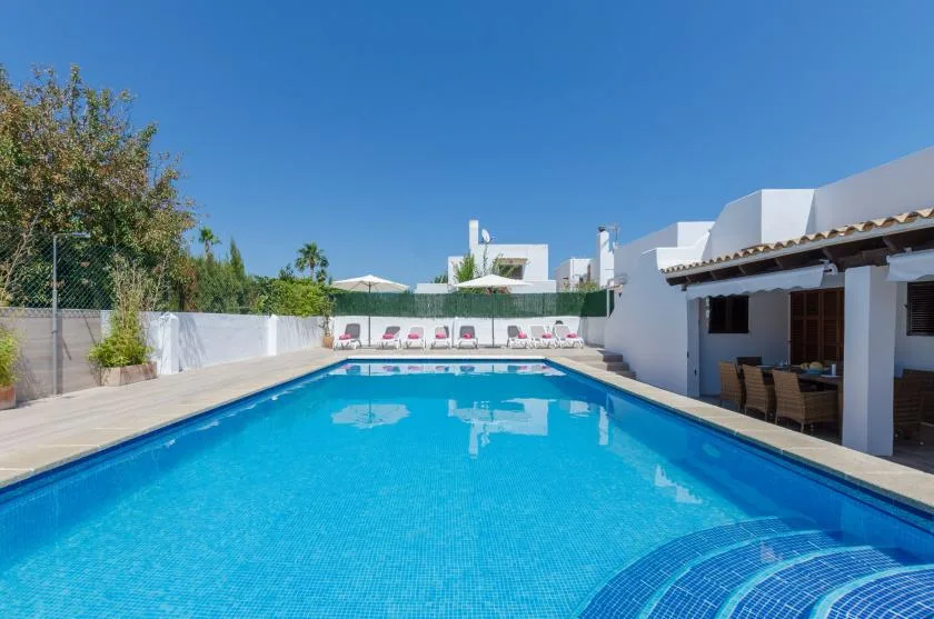 Una piscina al aire libre junto a un edificio blanco, con tumbonas al fondo.