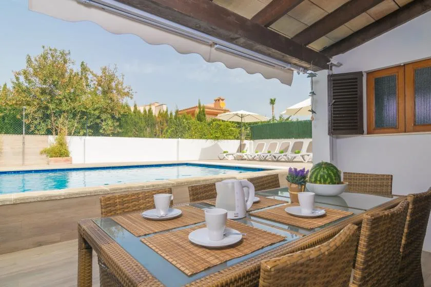 Una zona de comedor en un patio cubierto da a una piscina y un jardín.
