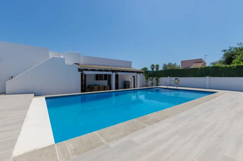 Una piscina al aire libre junto a un patio cubierto y paredes blancas.