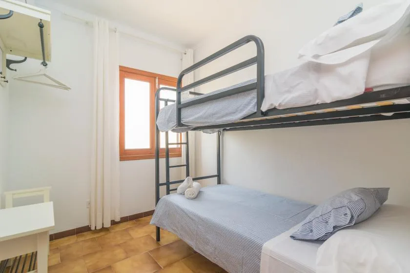 Un dormitorio con una litera metálica, ropa de cama gris y una ventana.