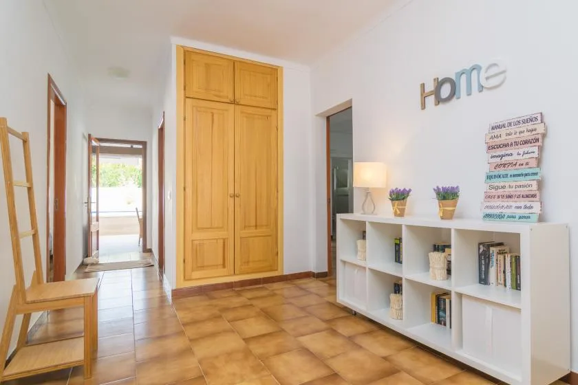 Un pasillo luminoso con un armario de madera y una estantería baja.