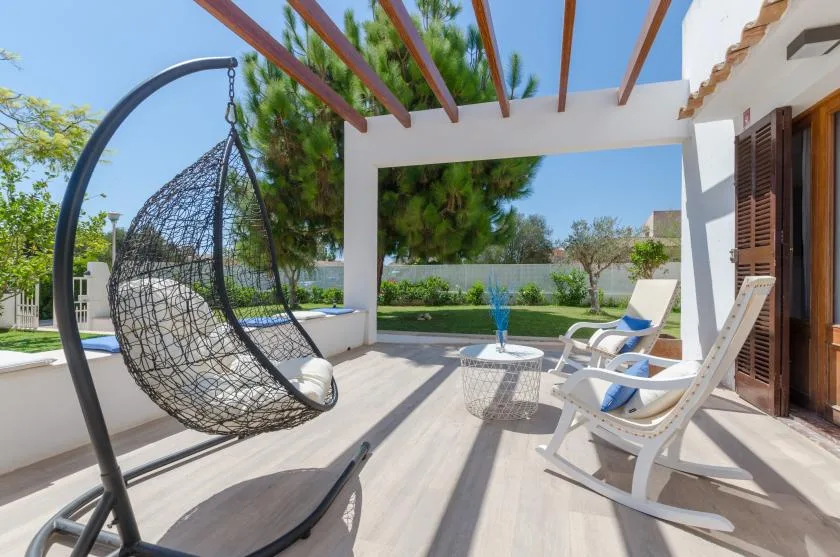 Un patio soleado con asientos al aire libre y una silla colgante bajo una pérgola.