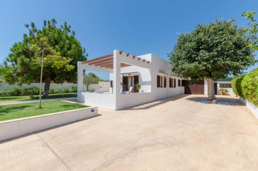 Una casa blanca moderna da a un amplio patio pavimentado con árboles.