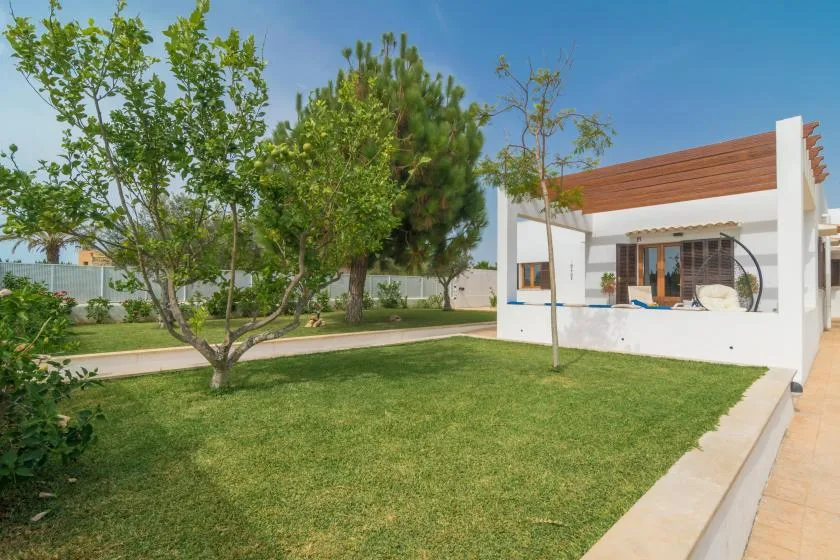 Un jardín ajardinado con árboles y césped junto a un edificio blanco moderno.