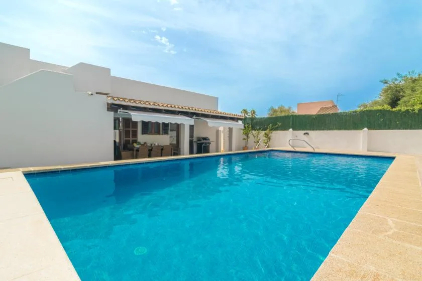 Piscina exterior junto a un edificio blanco, con un patio cubierto.