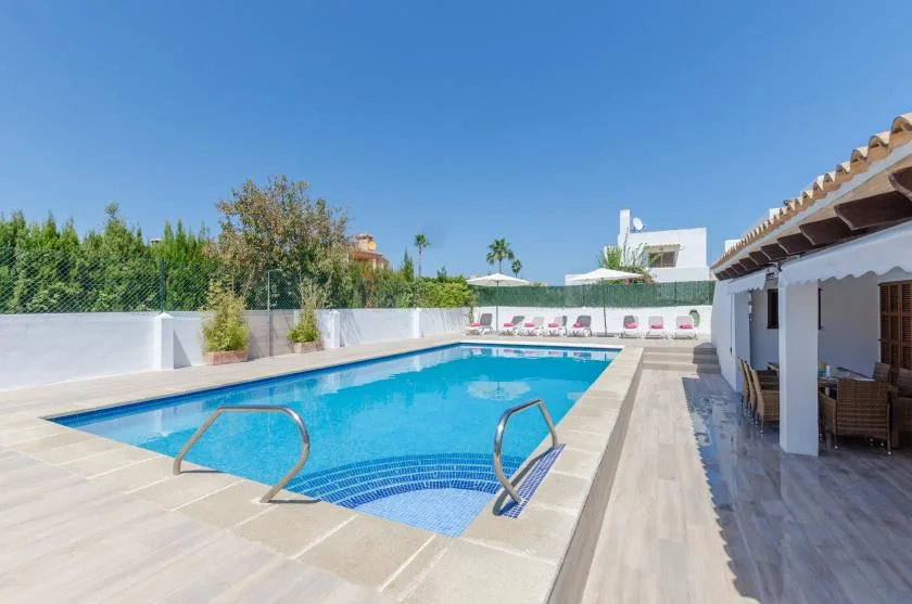 Piscina exterior junto a un patio cubierto con asientos.