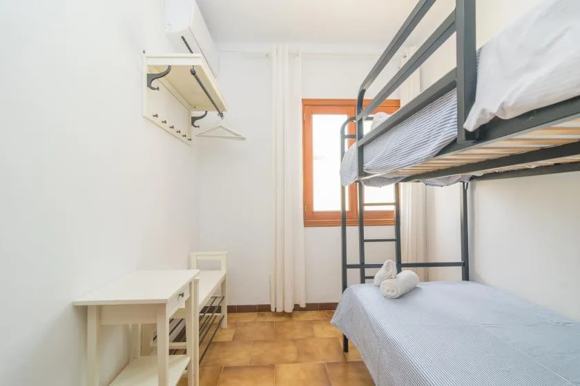 Un dormitorio luminoso con literas, una mesa pequeña y una ventana.