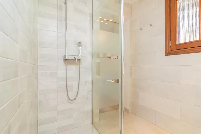 Un baño alicatado con una ducha de vidrio y una ventana con marco de madera.
