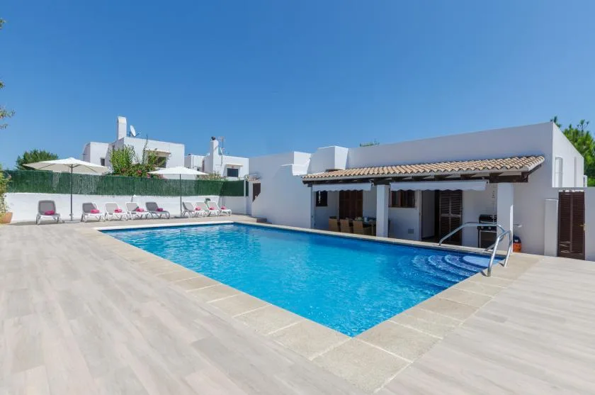 Una piscina junto a un edificio blanco, con asientos de descanso al fondo.