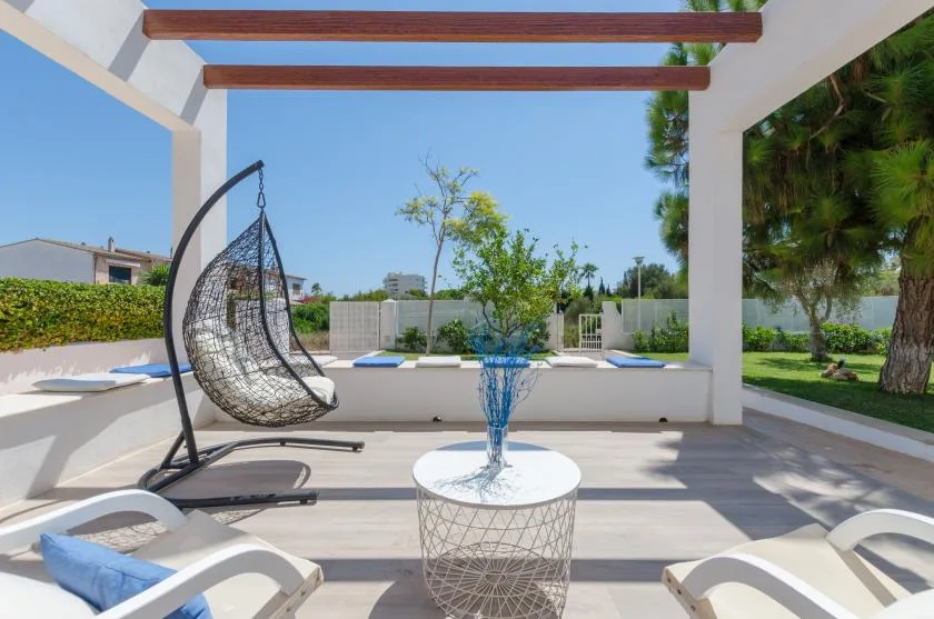 Un patio exterior a la sombra con un asiento colgante y una mesa redonda pequeña.