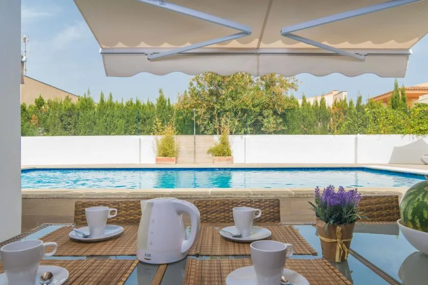 Una mesa en el patio junto a la piscina está bajo un toldo, con la piscina al fondo.