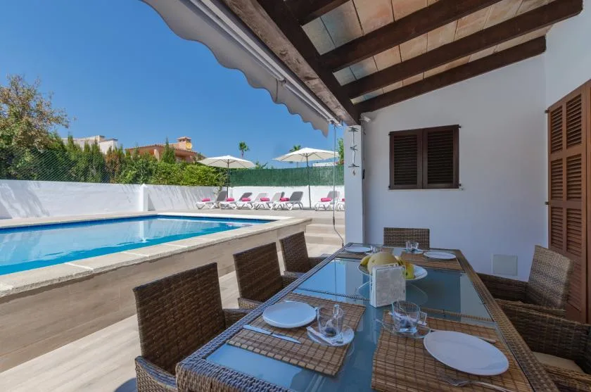 Una zona de comedor exterior cubierta da a una piscina y varias tumbonas.