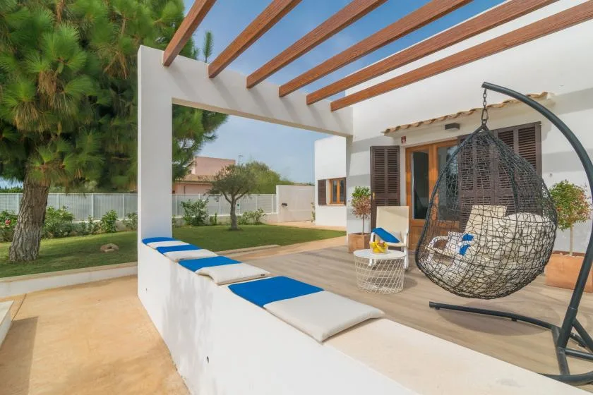 Un patio soleado con una silla colgante, asientos acolchados y vigas de madera.