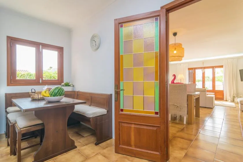 Un rincón de comedor con asientos de madera y una puerta de paneles de vidrio coloridos hacia la sala.
